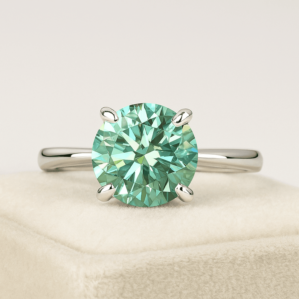 Teal round moissanite solitaire ring on a soft velvet jewelry box